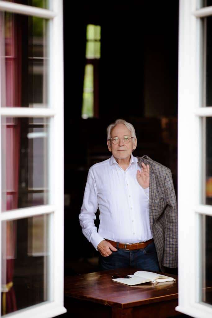Personal Branding Foto eines Psychologen der vor einem Tisch steht mit Buch und Stift und ein Sakko über der Schulter trägt